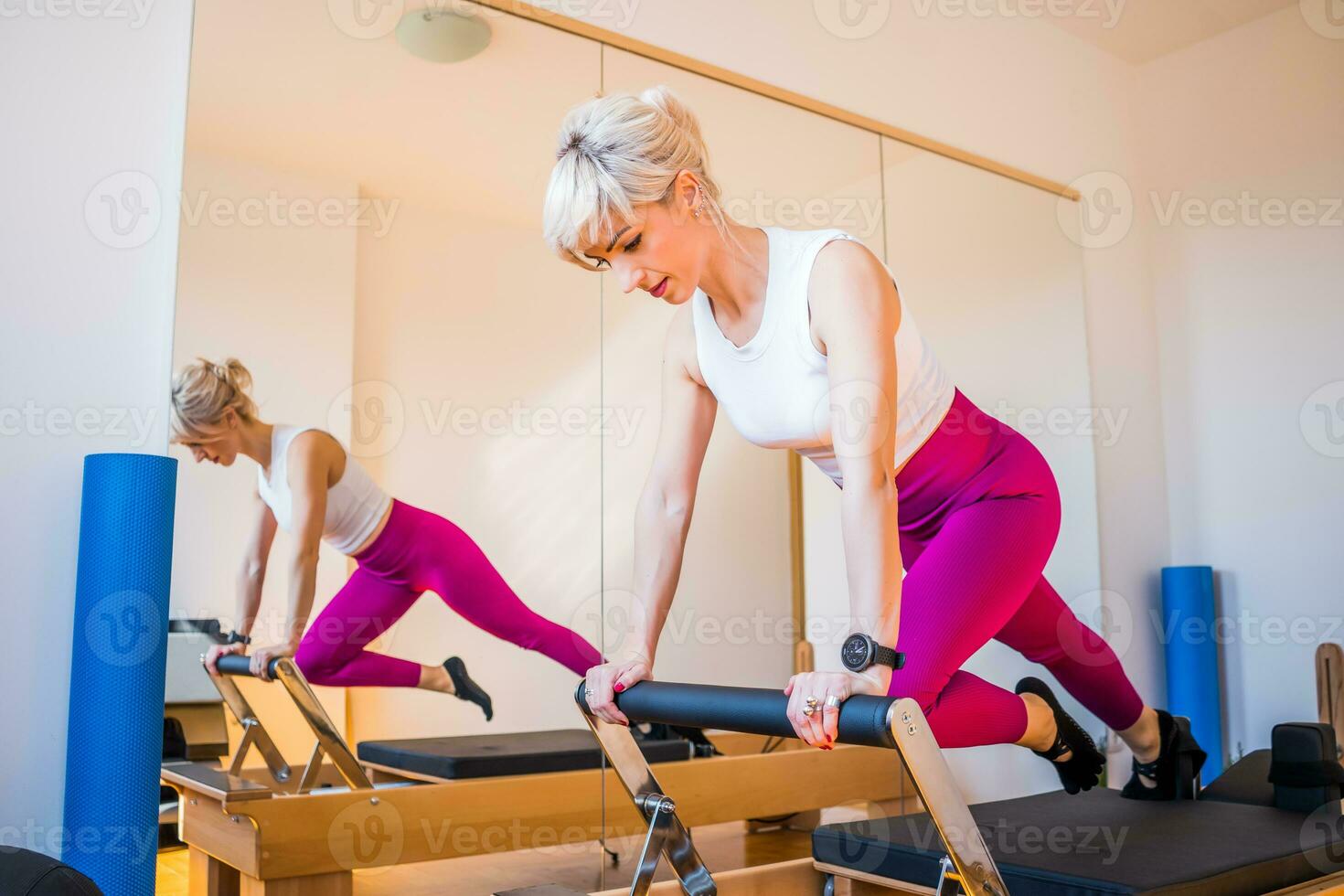 blond kvinna är utövar på pilates reformator säng i henne Hem. foto