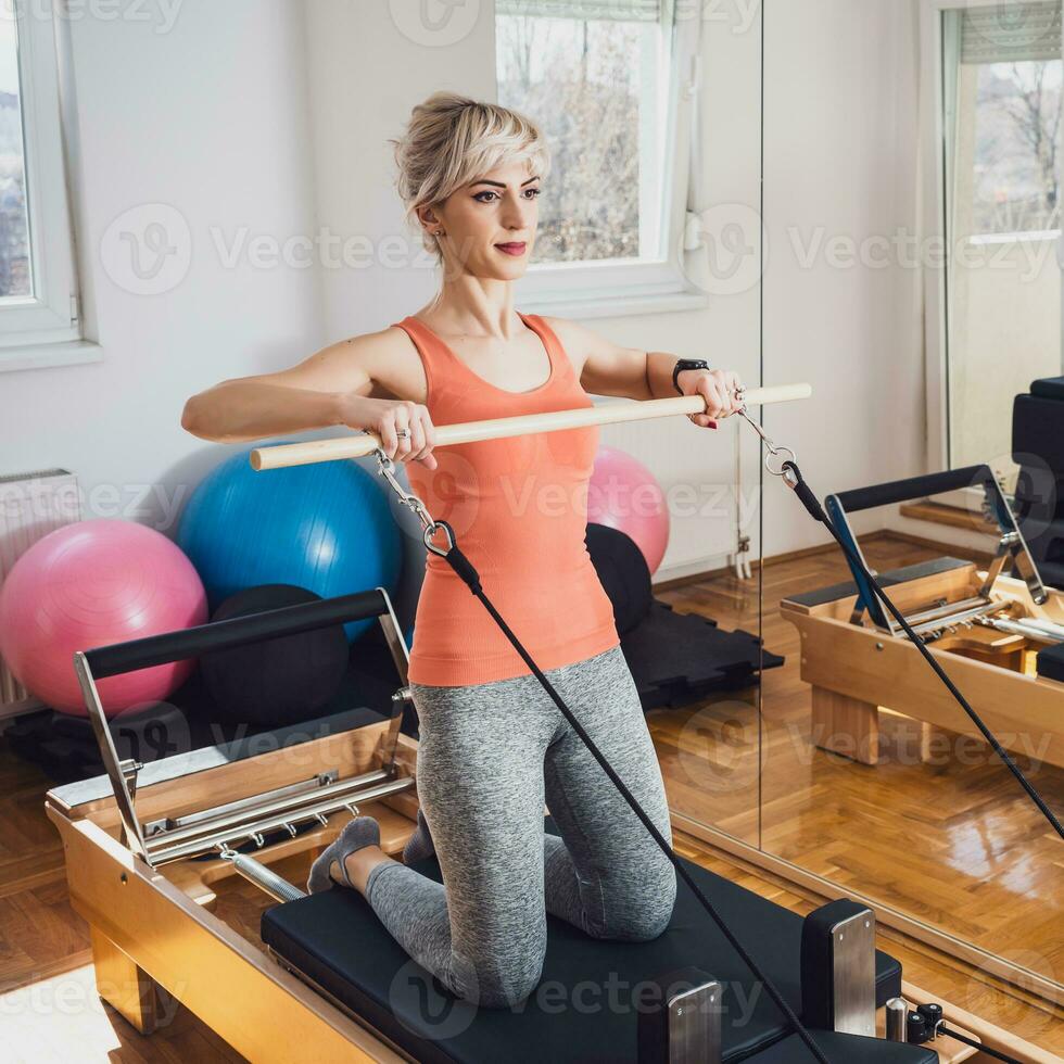 blond kvinna är utövar på pilates reformator säng i henne Hem. foto