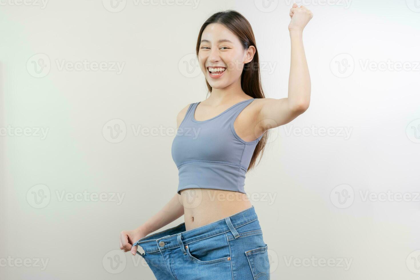 form smal, tunn midja, attraktiv smal asiatisk ung kvinna, hand visa form henne vikt förlust, bär i stor, stor eller oversize jeans, överskott tappa bort förbi diet och träning. människor kropp passa friska. foto