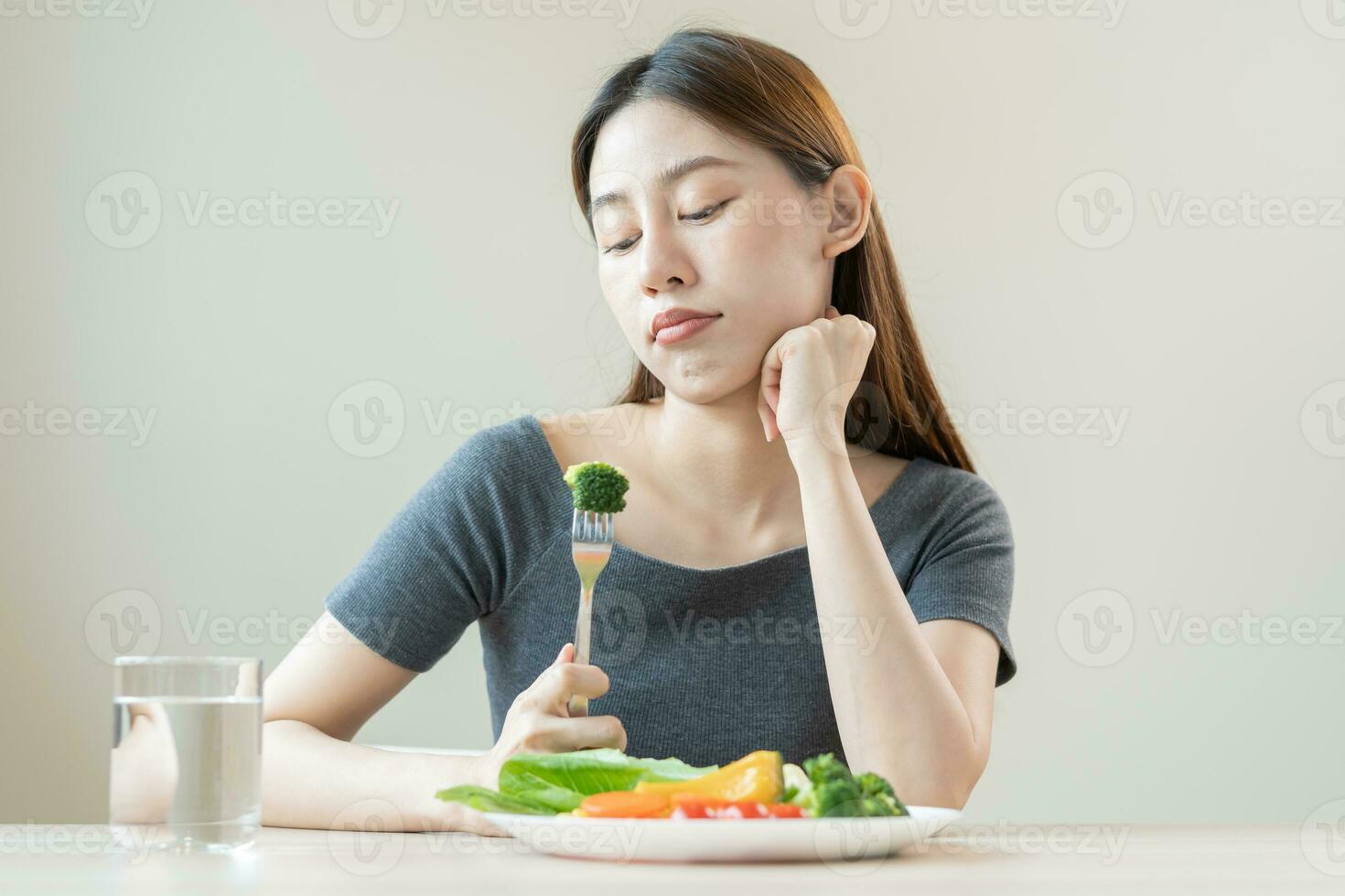 diet i uttråkad, olycklig skön asiatisk ung kvinna, flicka på bantning, innehav gaffel på broccoli i sallad tallrik, motvilja eller trött med äta färsk grönsaker. näring av rena, friska mat Bra smak. foto