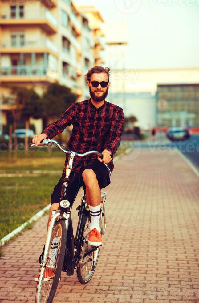 eleganta man i solglasögon ridning en cykel på stad gata foto