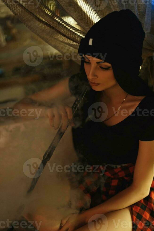 skön ung hipster flicka i stickat hatt röker en vattenpipa foto