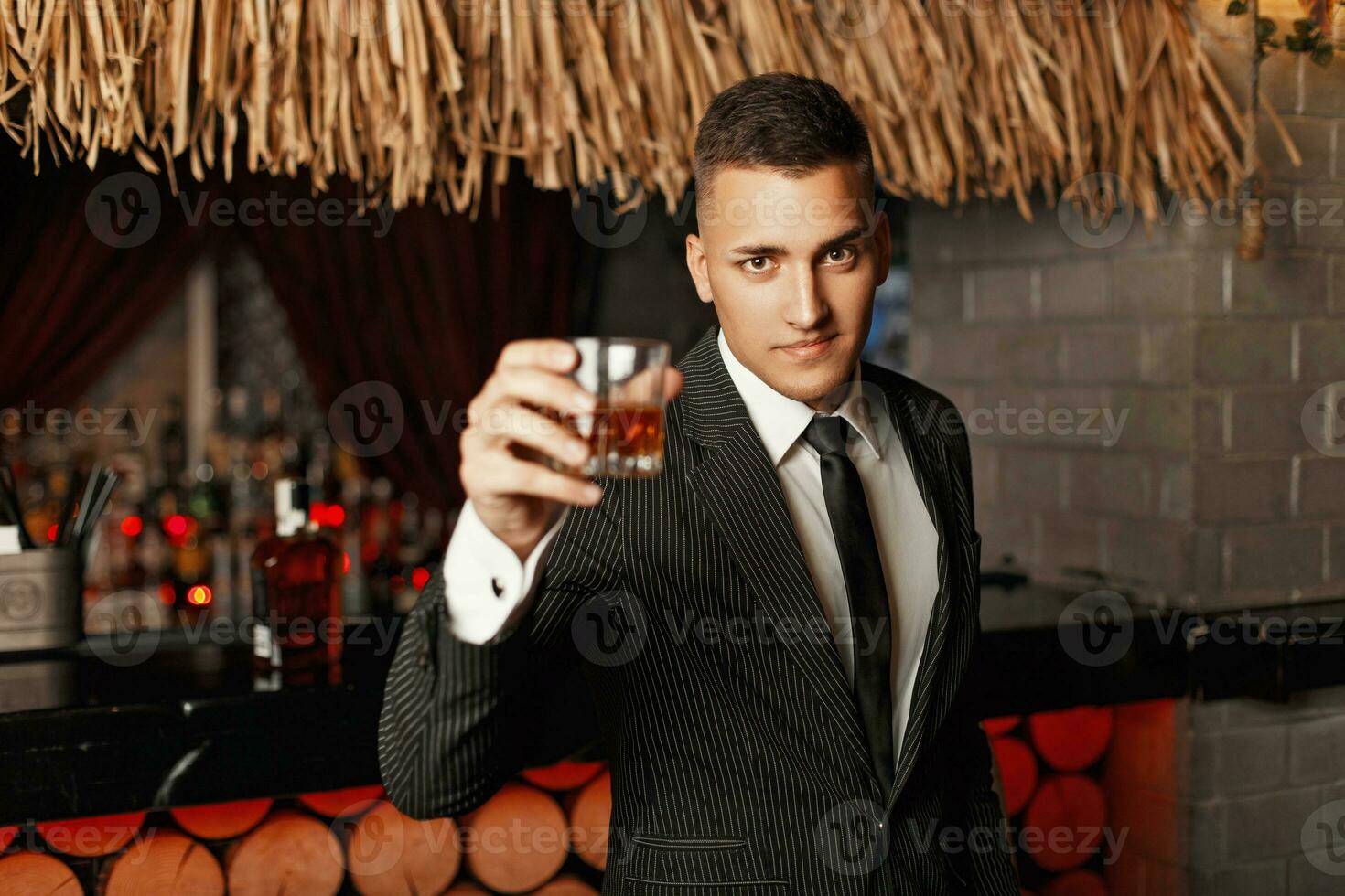 stilig ung man i en eleganta kostym dricka whisky i de bar. foto