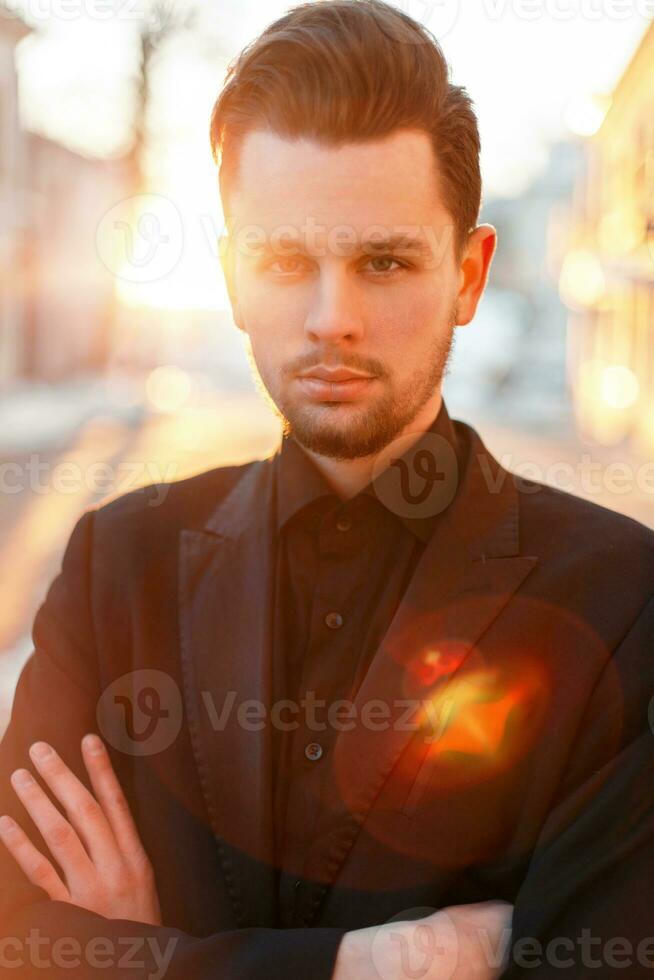 stilig man med en skägg och frisyr i svart elegant kostym på solnedgång foto