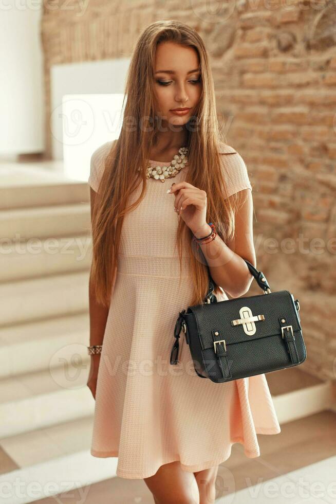 skön elegant kvinna i en rosa klänning med en väska kommer ner de trappa. foto