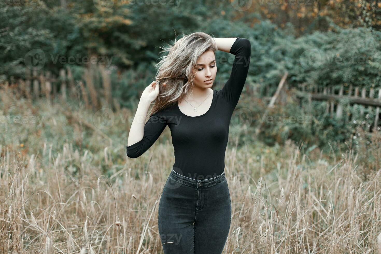 skön flicka med hår i en svart skjorta och svart jeans stående i en fält med gräs. foto
