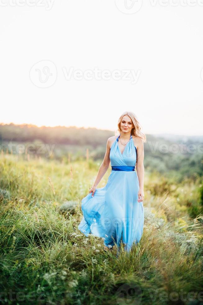 blond tjej med löst hår i en ljusblå klänning och en kille i solnedgångens ljus foto