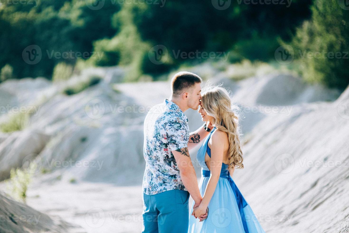 blond tjej i en ljusblå klänning och en kille i en ljus skjorta i ett granitbrott foto