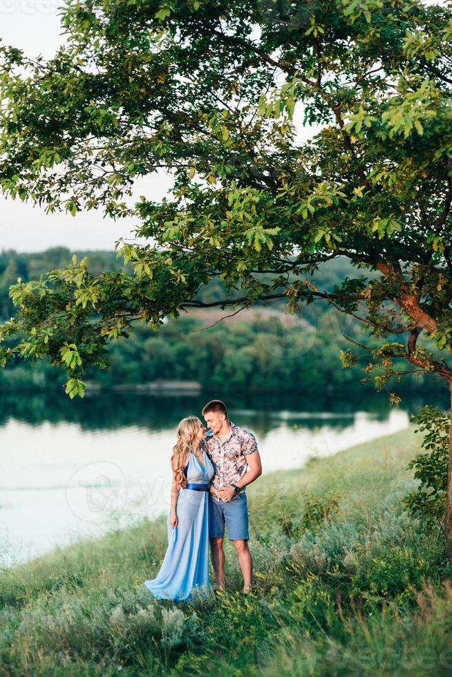 blond tjej med löst hår i en ljusblå klänning och en kille i solnedgångens ljus foto