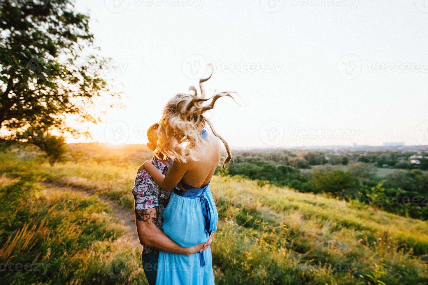 blond tjej med löst hår i en ljusblå klänning och en kille i solnedgångens ljus foto