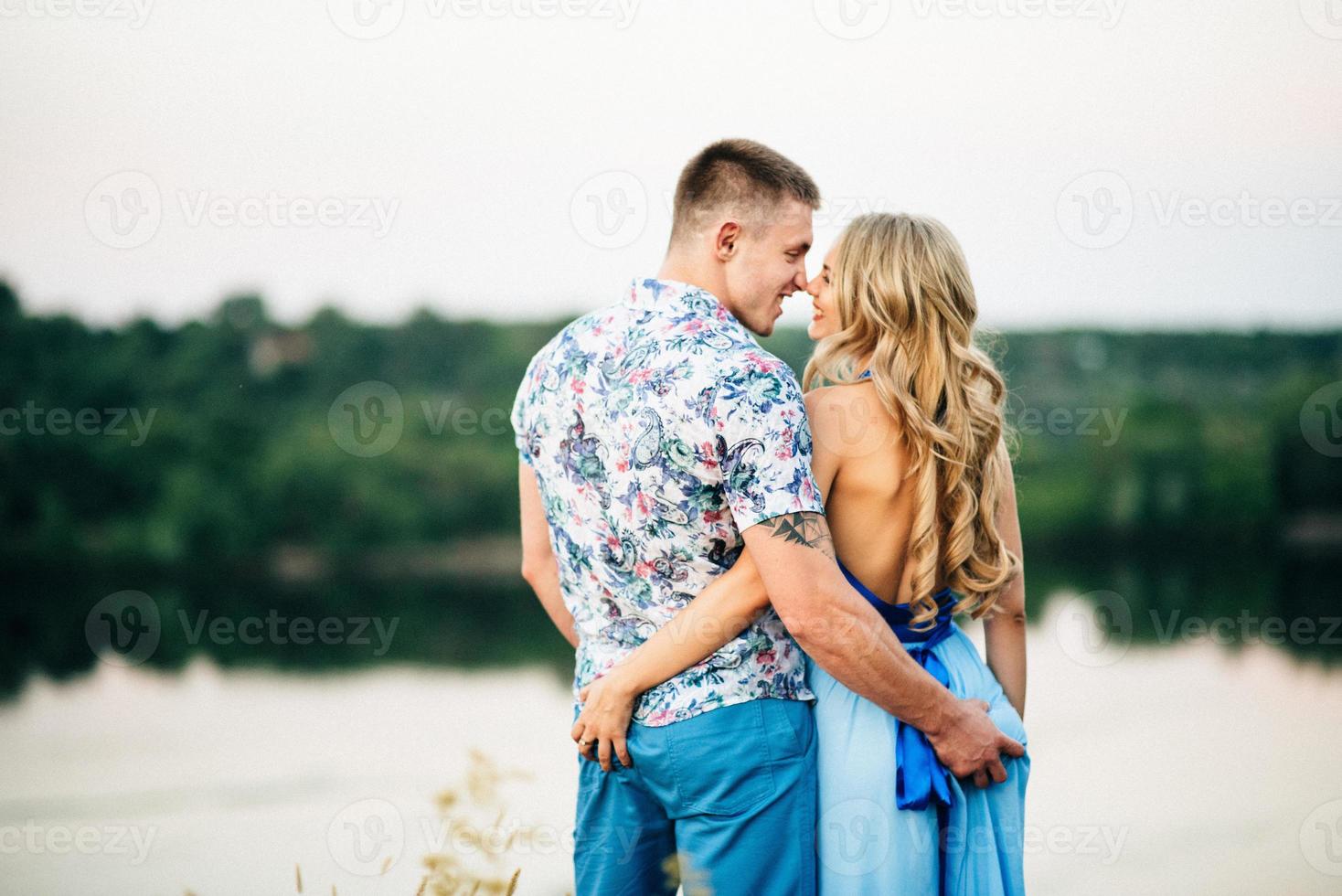 blond tjej med löst hår i en ljusblå klänning och en kille i solnedgångens ljus foto