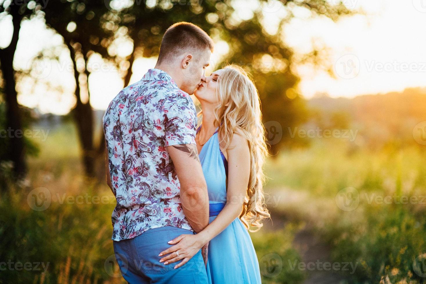 blond tjej med löst hår i en ljusblå klänning och en kille i solnedgångens ljus foto