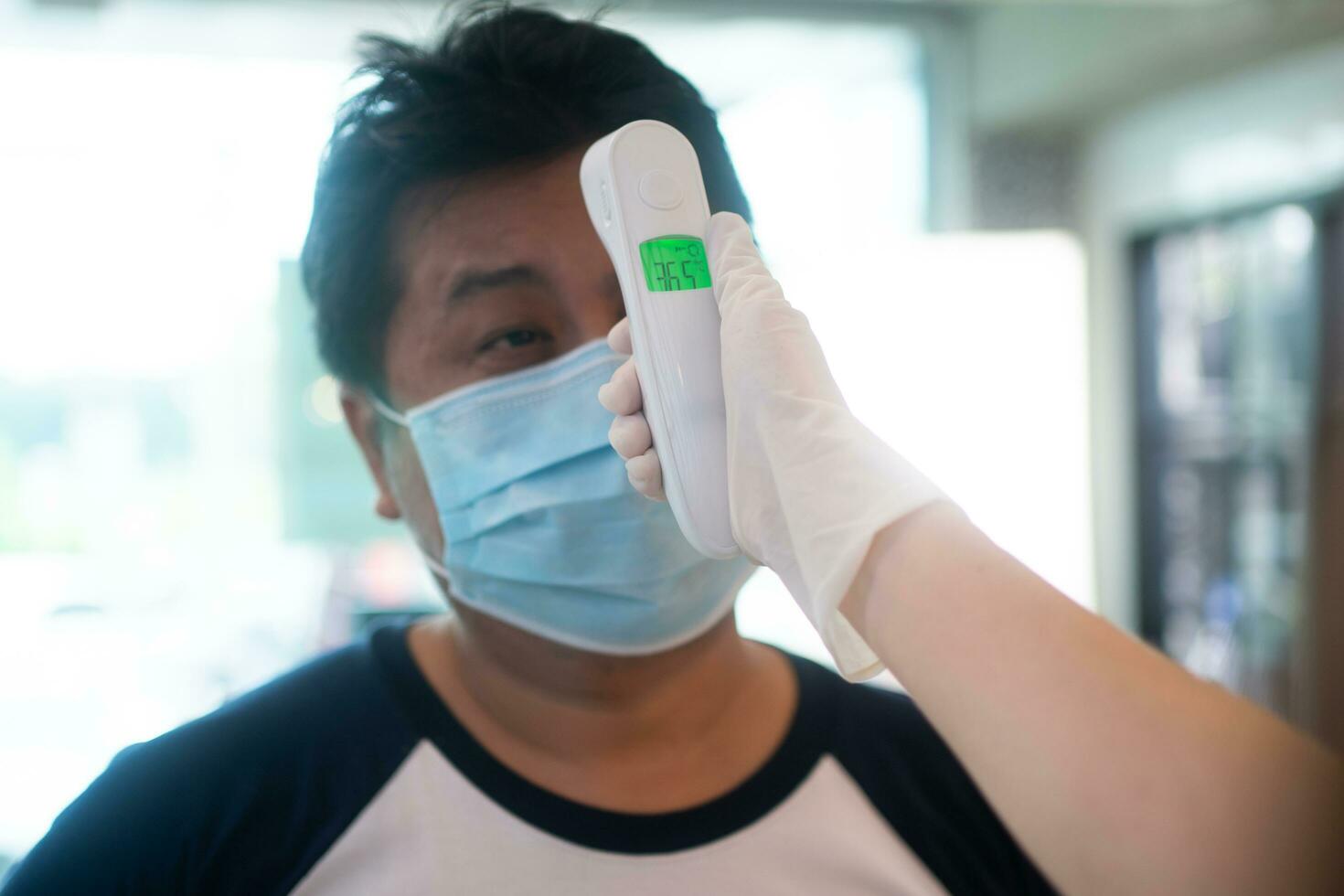 asiatisk servitris kvinna bär ansikte masker och innehav ett infraröd panna termometer till kolla upp kropp temperatur för virus symptom av kunder innan som förs in i de restaurang kaffe affär. foto