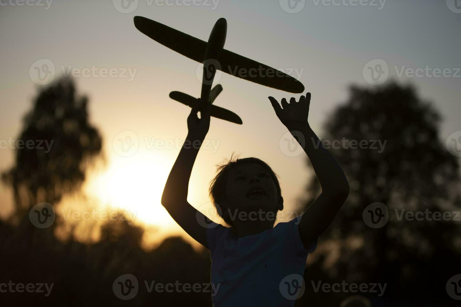 Lycklig barn spelar med ett flygplan på solnedgång. silhuett av en pojke med ett flygplan på de bakgrund av de Sol. foto