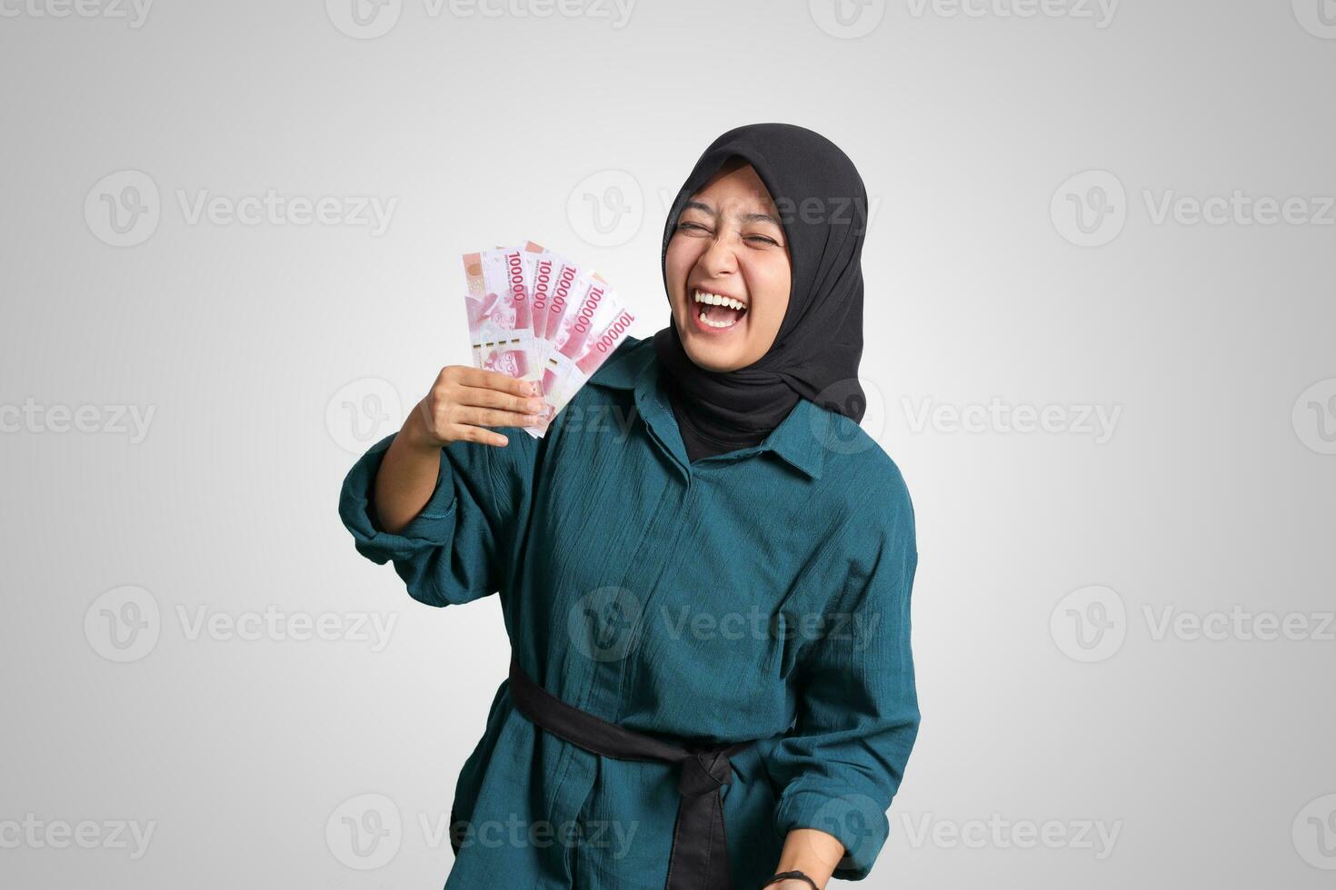 porträtt av upphetsad asiatisk hijab kvinna i tillfällig utrusta som visar ett hundra tusen rupiah. finansiell och besparingar begrepp. isolerat bild på vit bakgrund foto