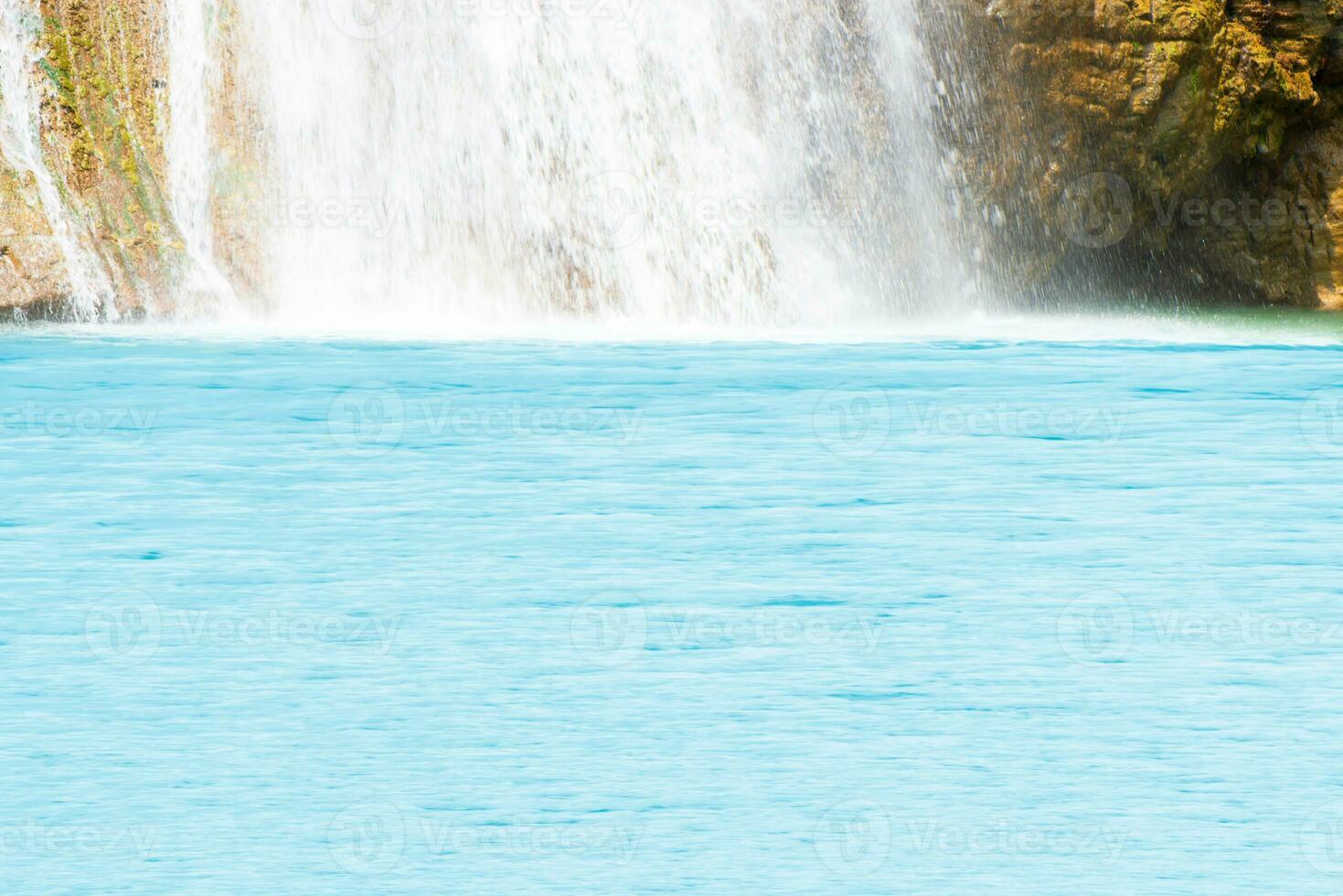 skön vattenfall i skogsbruk med blå vatten med krusningar på de yta. suddig transparent blå färgad klar lugna vatten yta textur med stänk och bubblor. vatten vågor med lysande. foto