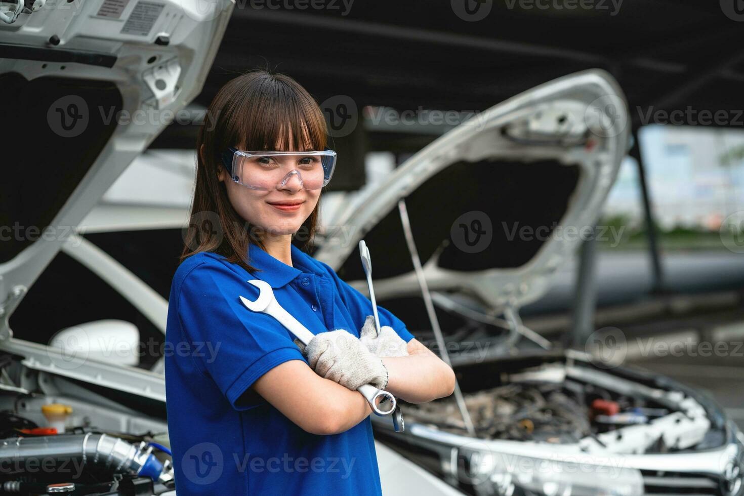 bilverkstad, en glad kvinnlig mekaniker som står vid bilen. asiatisk kvinna bilmekaniker bär akvarell skjorta i garaget. glad kvinna mekaniker i auto reparation servicecenter. foto