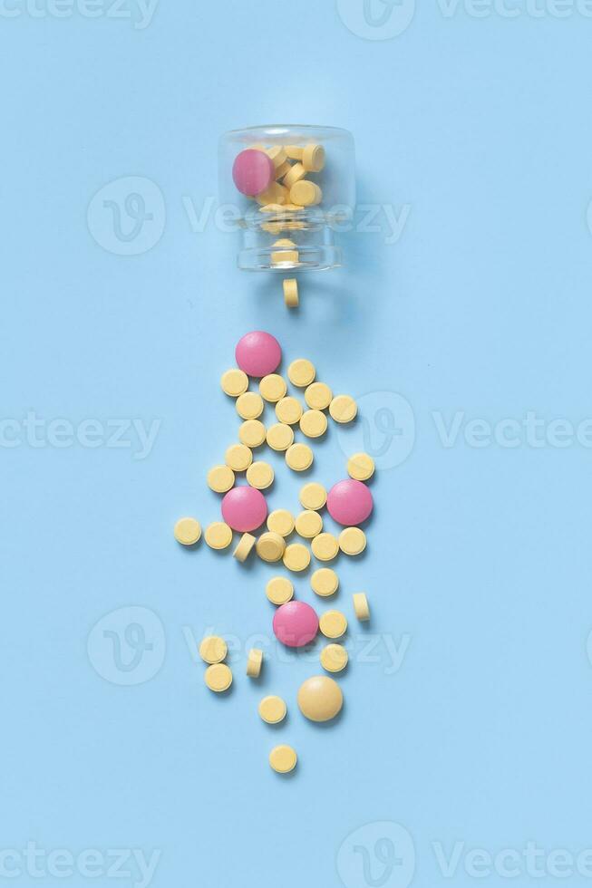 färgrik piller med glas flaska på blå bakgrund. sjukvård och medicin bakgrund platt lägga foto