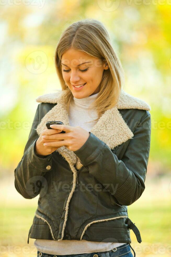 kvinna på läder jacka innehav de telefon utomhus foto