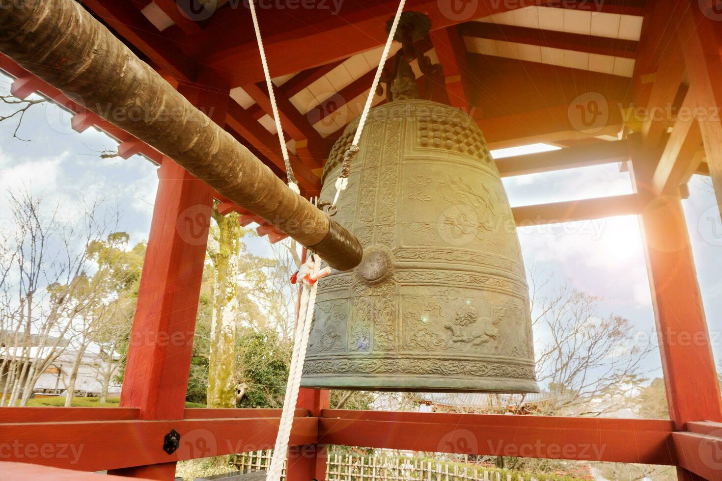 stor mässing buddist klocka och slå klocka timmer av japansk tempel i röd paviljong på ljus blå himmel med Sol och lins blossa bakgrund. foto