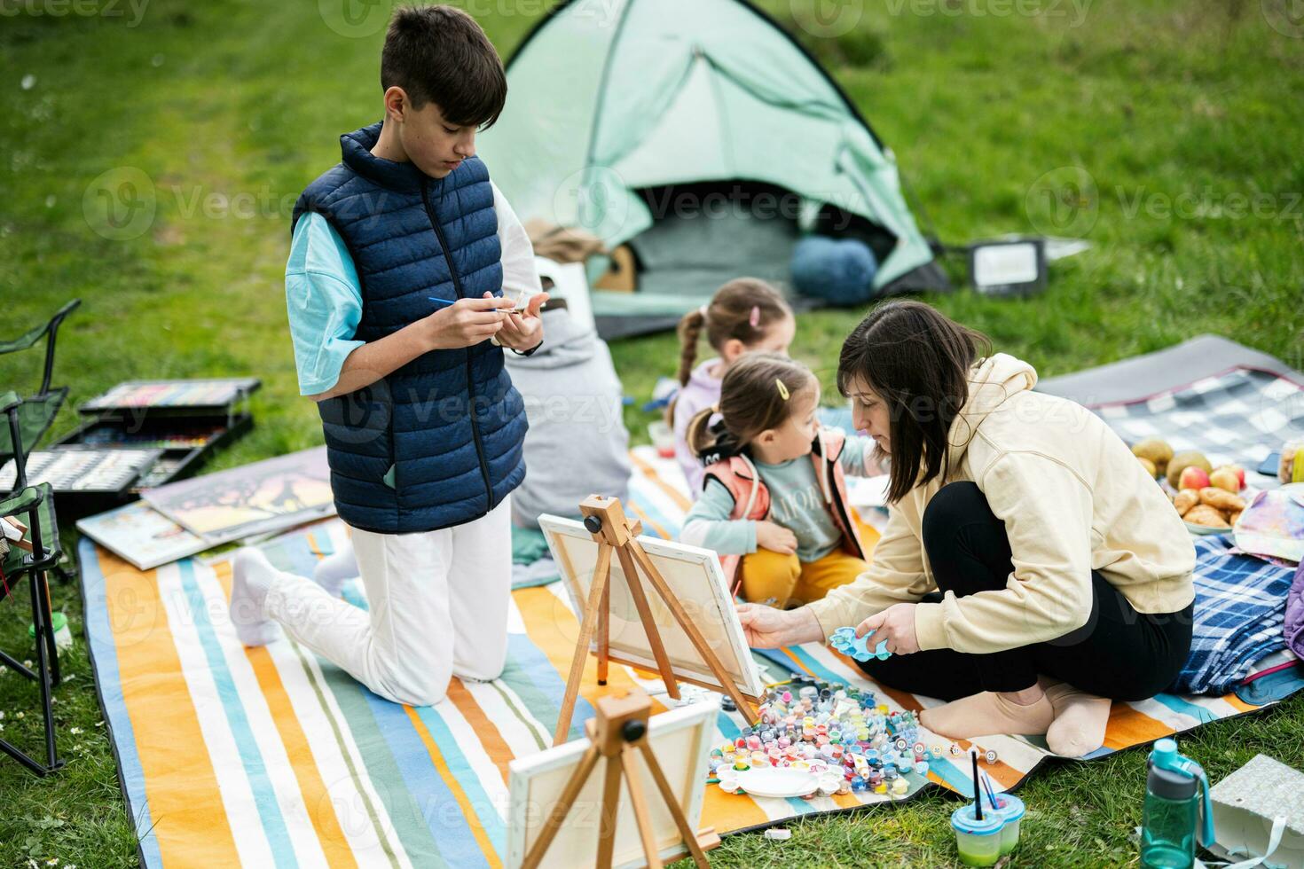 Lycklig ung familj, mor och barn har roligt och njuter utomhus- på picknick filt målning på trädgård vår parkera, avslappning. foto