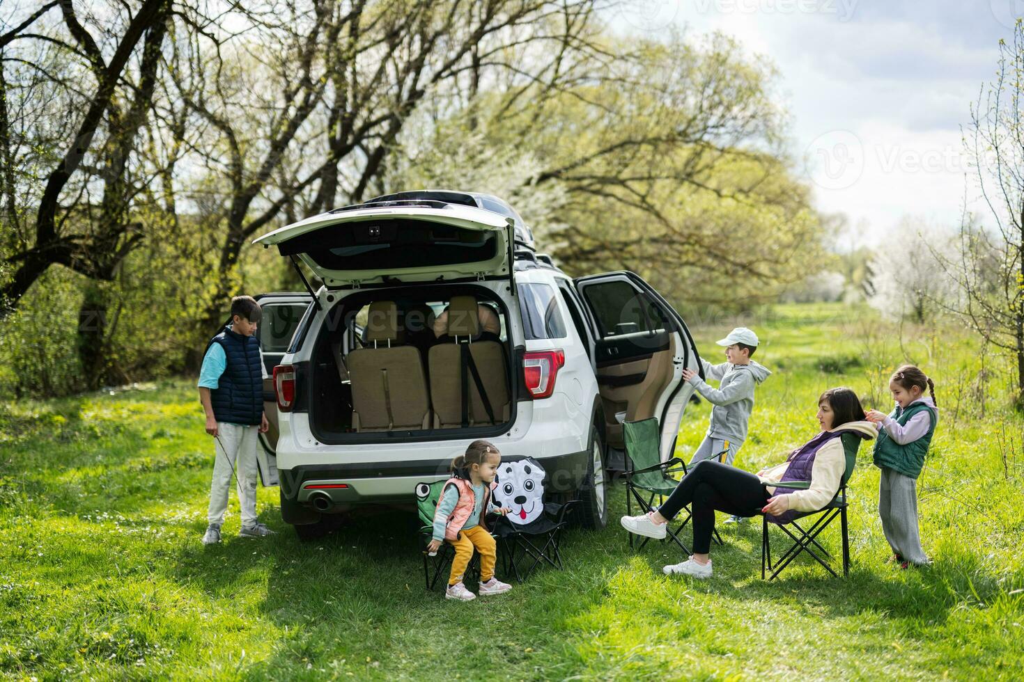 mor med barn sitta på stol mot bil öppen trunk på picknick. foto