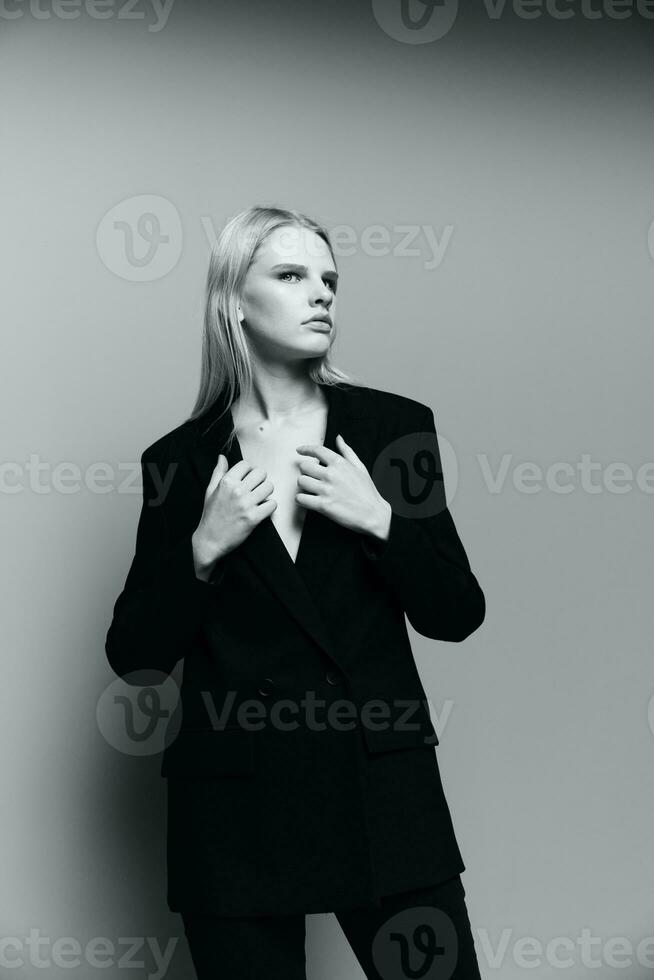 en eleganta lady i en kostym håller henne händer på de krage och sätter på en jacka i de studio. de begrepp för de ny samling. klassisk svart och vit Foto