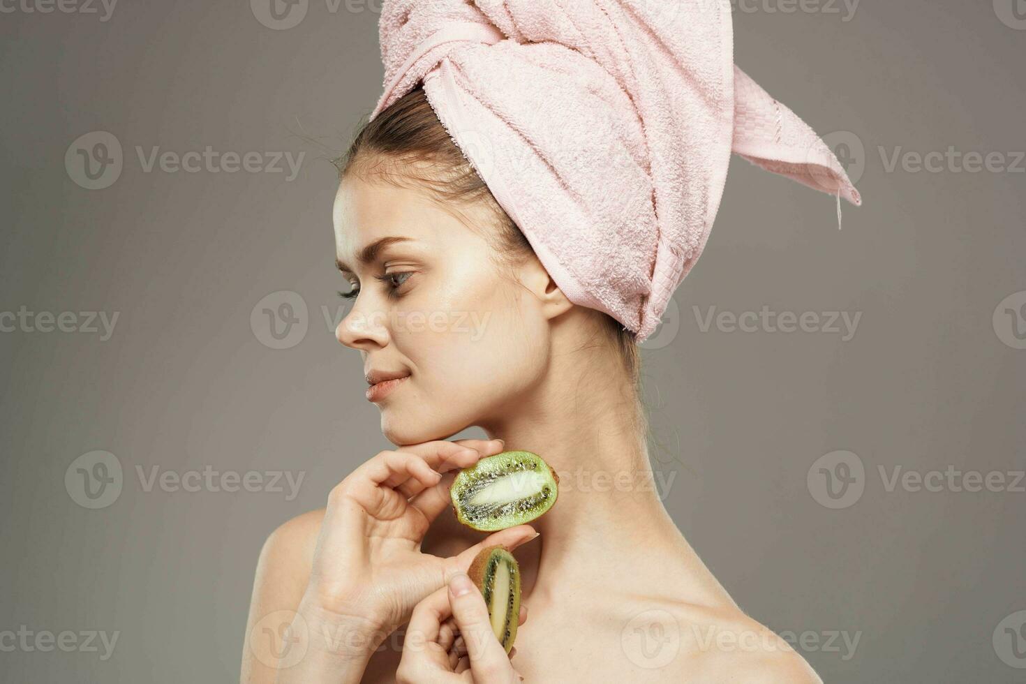 skön kvinna med rosa handduk på henne huvud naken axlar kiwi i händer hälsa hud vård foto