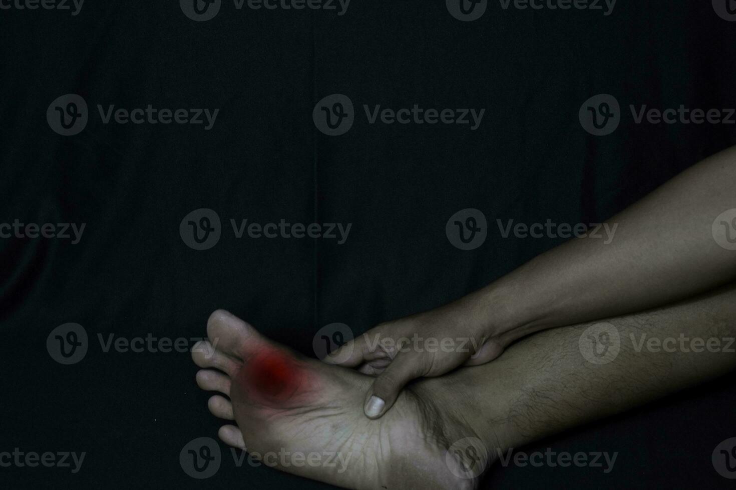 asiatisk man innehav hans fot. han känner smärta från majs på hans fot enda med svart bakgrund. medicinsk eller sjukvård begrepp foto