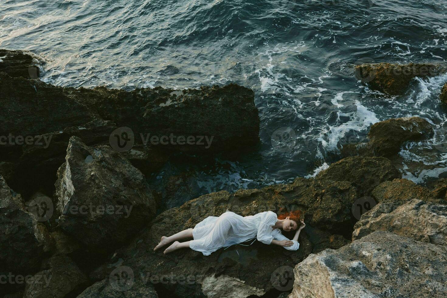 attraktiv kvinna med lång hår liggande på klippig kust med sprickor på klippig yta natur landskap foto