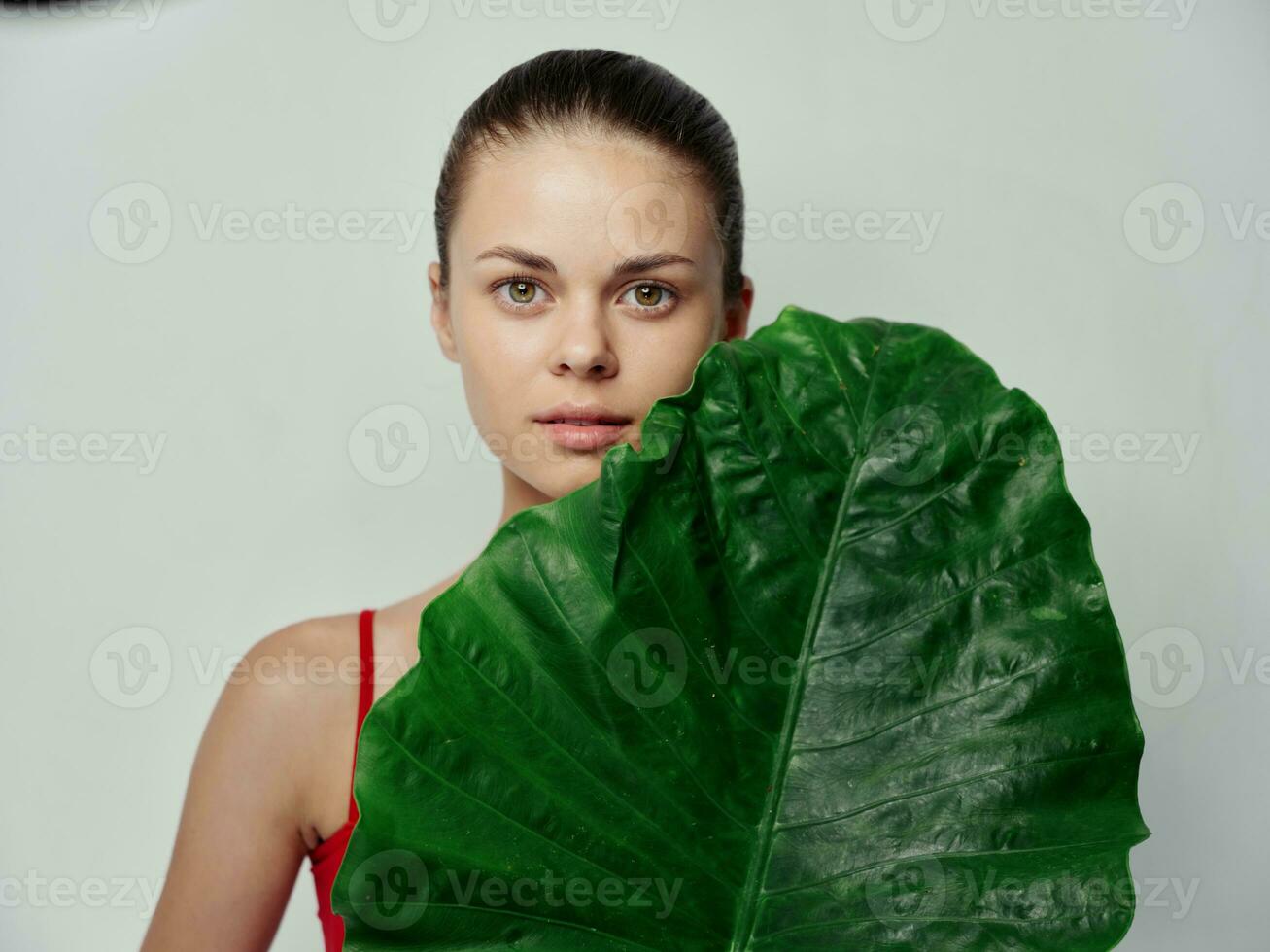 en kvinna i en röd t-shirt på en ljus bakgrund innehar en grön blad i henne händer fält foto