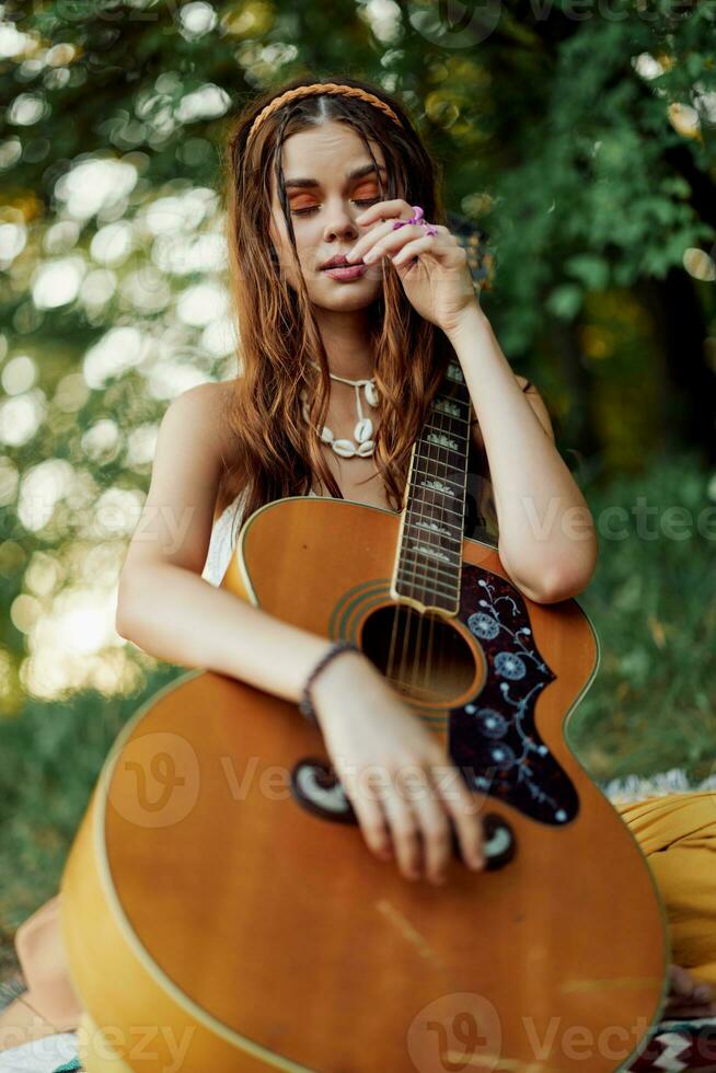 en ung hippie kvinna med en gitarr i henne händer ler sött in i de kamera på en resa till natur livsstil i harmoni foto