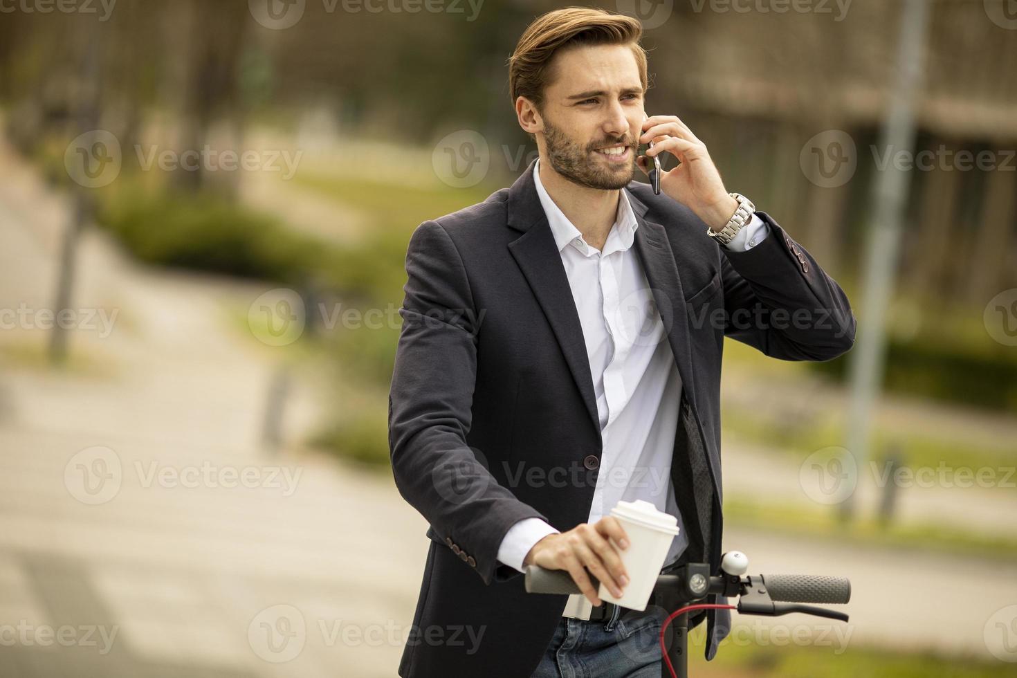 ung affärsman som använder mobiltelefonen på elektrisk skoter foto