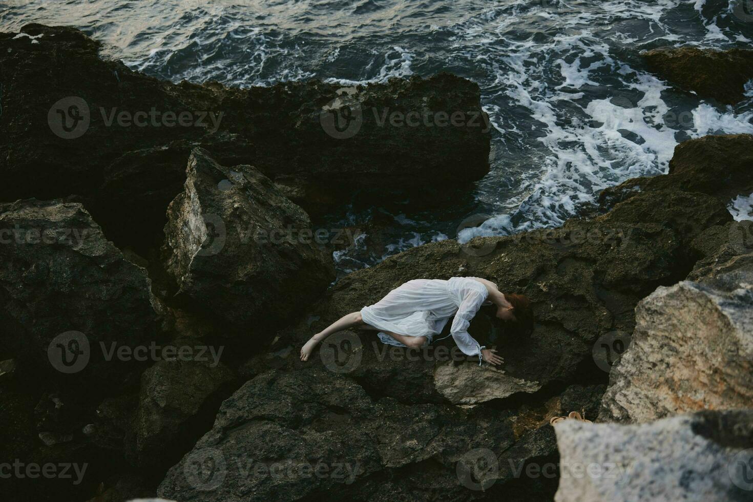 skön brud i lång vit klänning våt hår liggande på en klippig klippa landskap foto