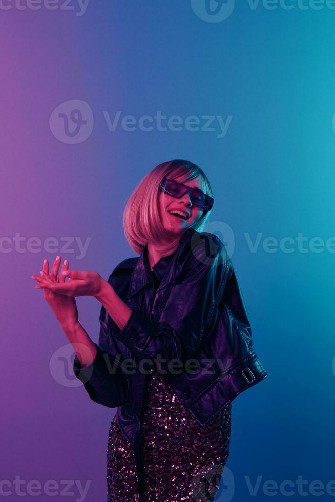 glad sexig skön blond kvinna i läder jacka glittrande klänning trendig solglasögon vika ihop händer Framställ isolerat i blå rosa Färg ljus studio bakgrund. neon fest cyberpunk begrepp. kopia Plats foto