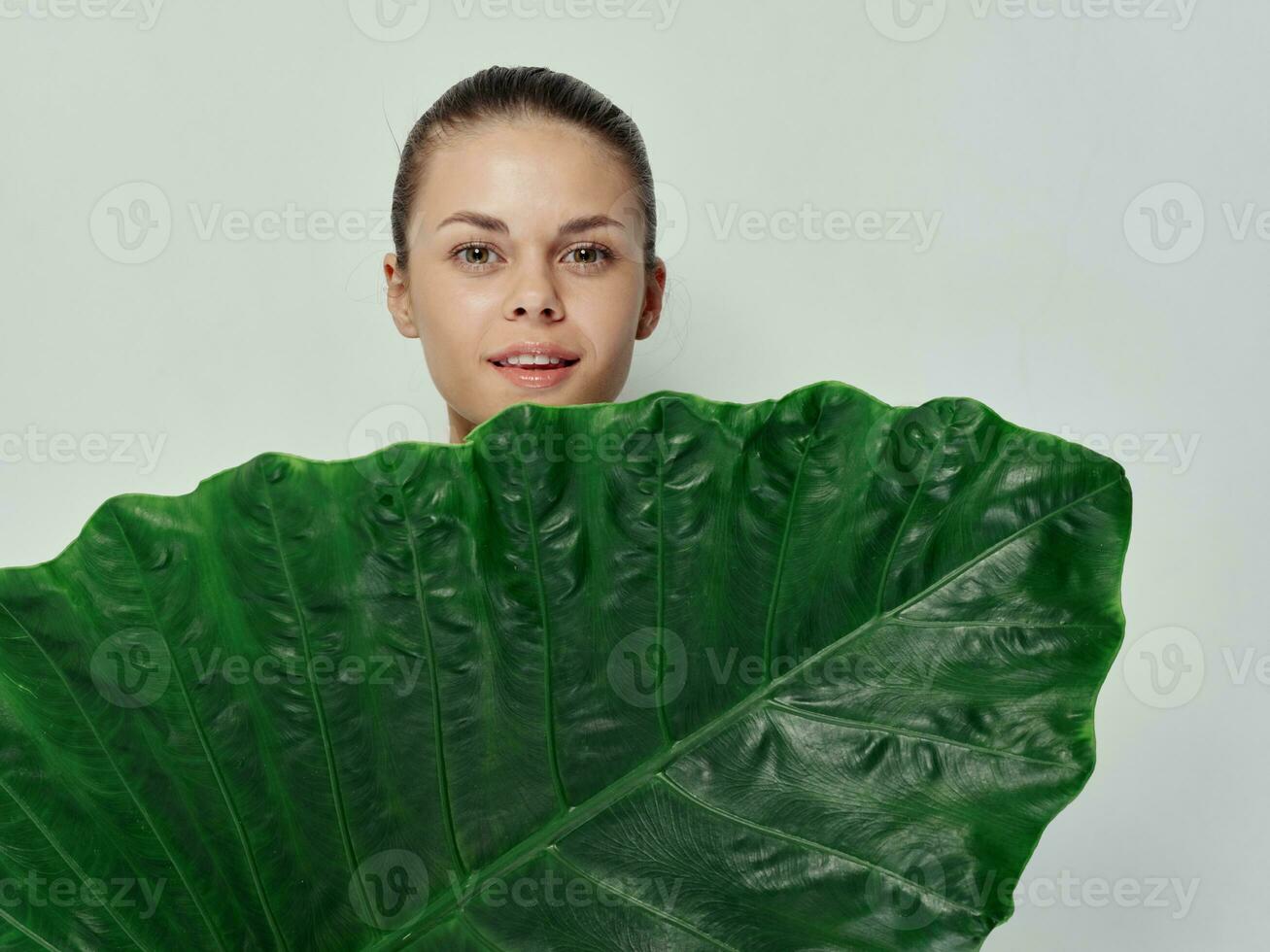 Söt kvinna omslag henne kropp med grön blad leende ljus bakgrund foto