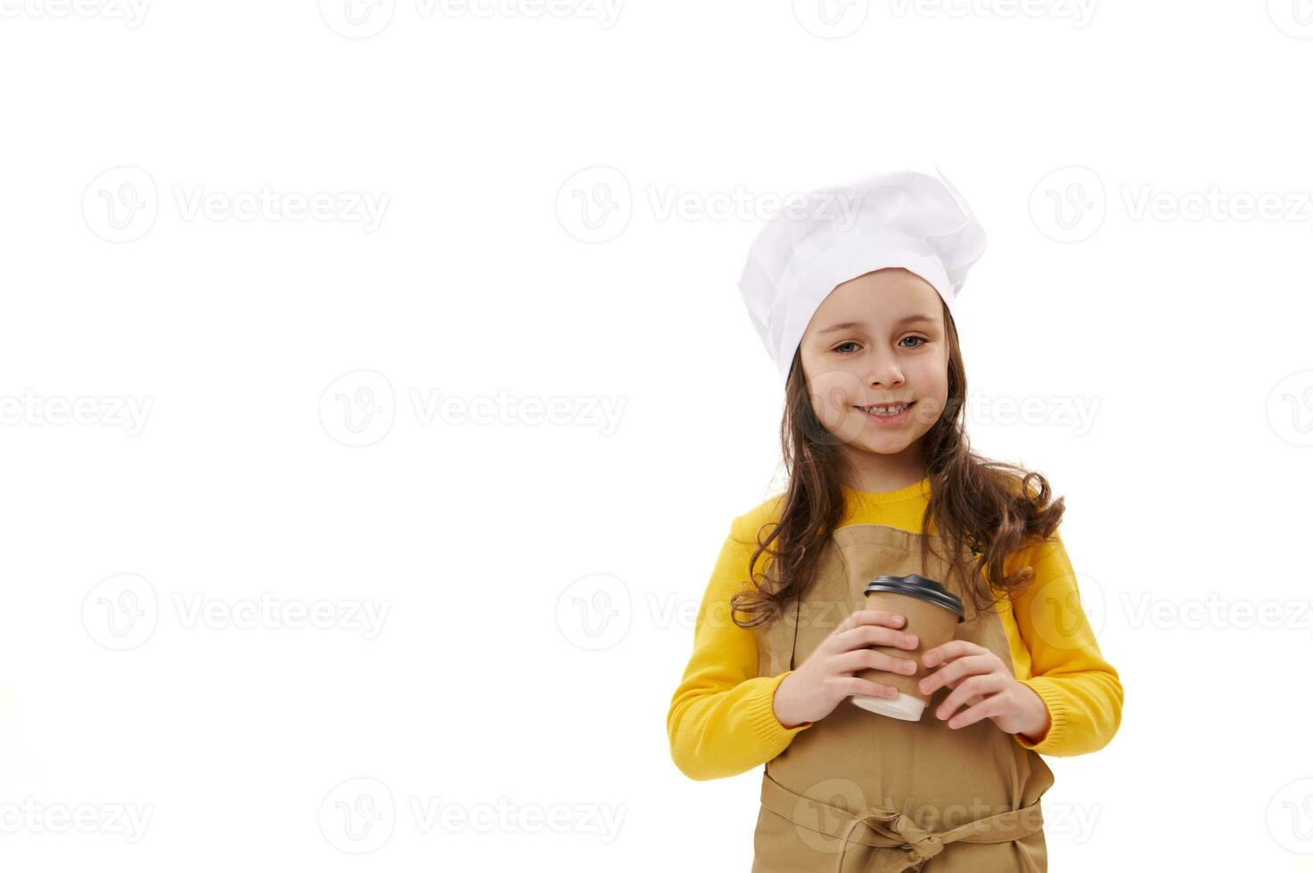 förtjusande leende liten unge flicka servitris i kockens hatt och förkläde, innehav en hämtmat varm dryck i återvinningsbar papper kopp foto