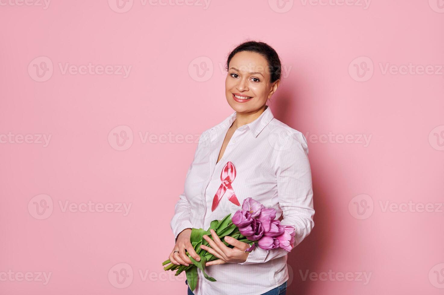 trevlig kvinna med bukett av tulpaner, bär rosa satin medvetenhet band, som visar Stöd för bröst cancer överlevande foto