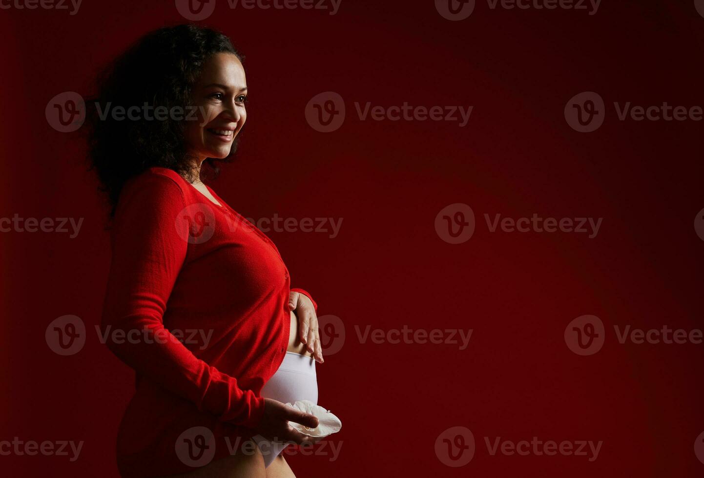 härlig vuxen gravid kvinna innehav vit orkide blomma, leende, smeksam henne mage, uttrycker positiv känslor foto