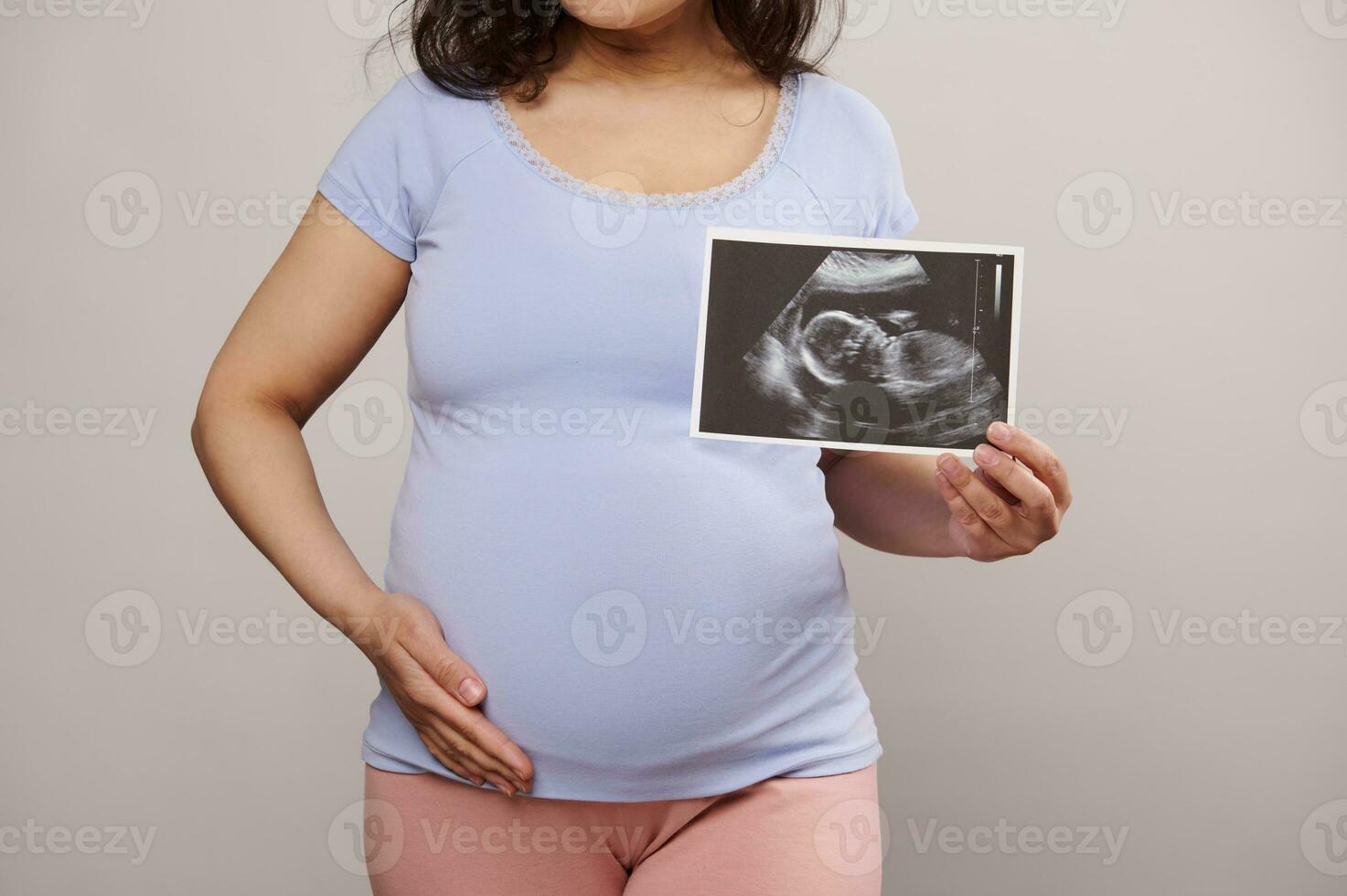 beskurna se gravid kvinna smeksam henne mage, som visar på kamera de nyfödd bebis ultraljud skanna över vit bakgrund foto