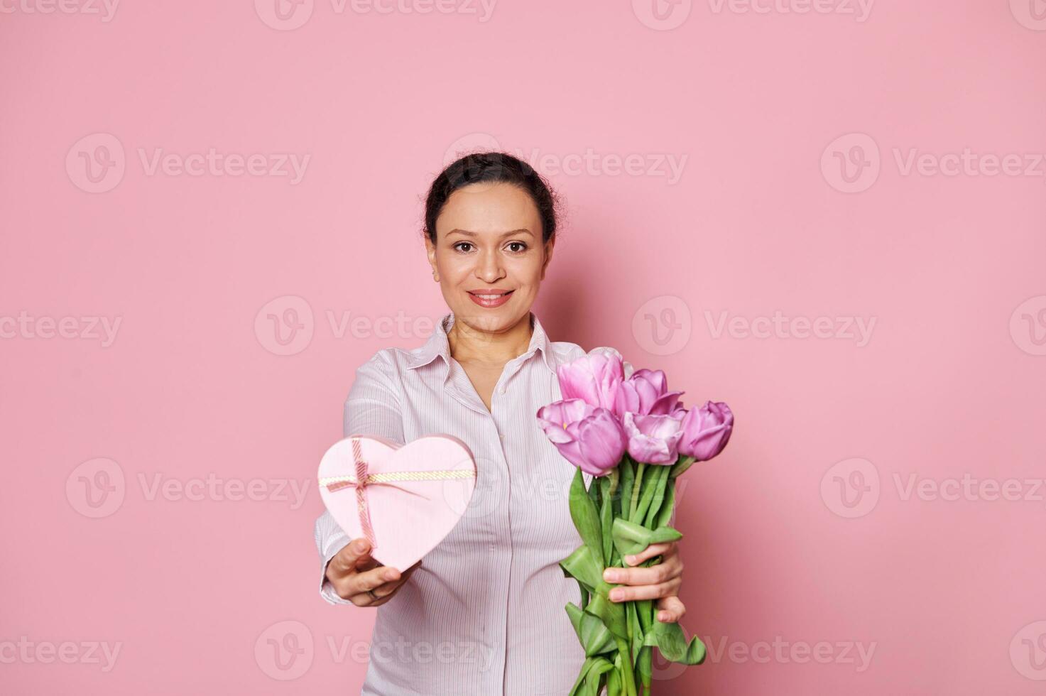 medelålders Söt kvinna innehav ut på kamera en bukett av tulpaner och hjärta formad gåva låda, hälsning med mors dag foto