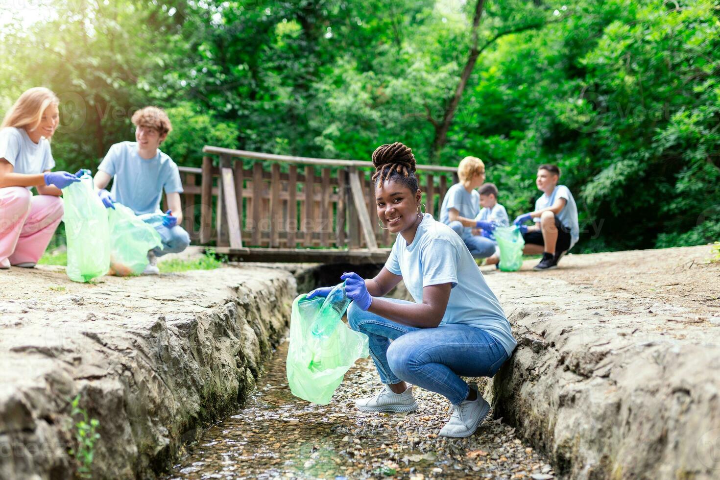 natur rengöring, volontär- ekologi grön begrepp. ung kvinna plocka upp flod på solnedgång . miljö plast förorening. sida se av en kvinna i skyddande handskar sätta hushåll avfall in i väska. foto