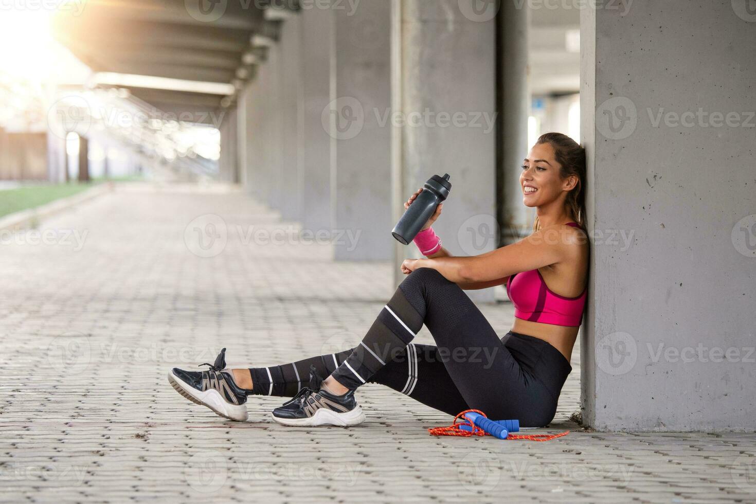 kondition kvinna avkopplande efter övning med en vassle protein flaska. avkopplande efter Träning. skön ung kvinna ser bort medan vilar efter löpning foto