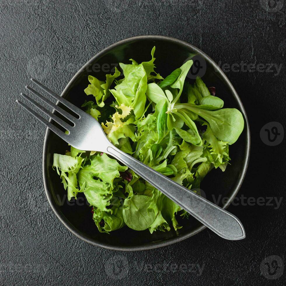grön sallad löv i skål på svart tabell. foto