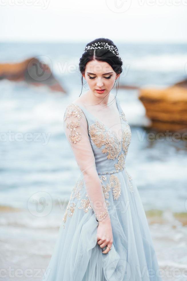 brud i en blå ljus klänning som går längs havet foto
