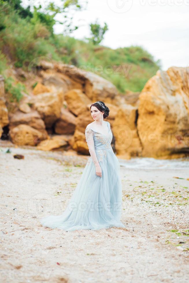 brud i en blå ljus klänning som går längs havet foto