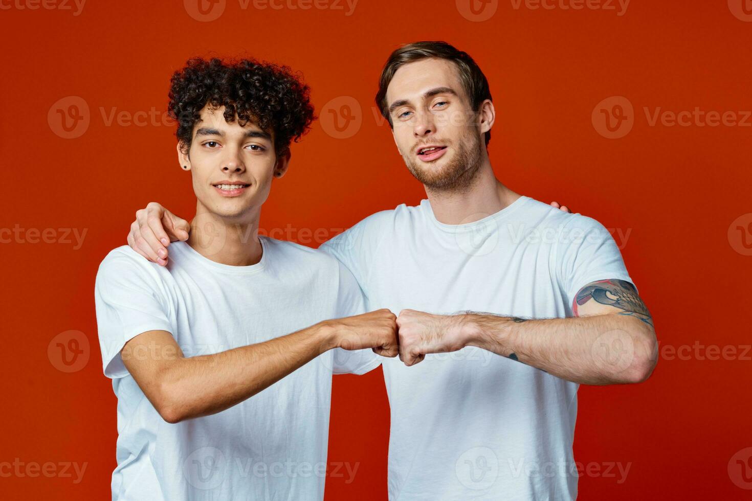 två vänner i vit t-tröjor kramar kommunikation röd bakgrund foto