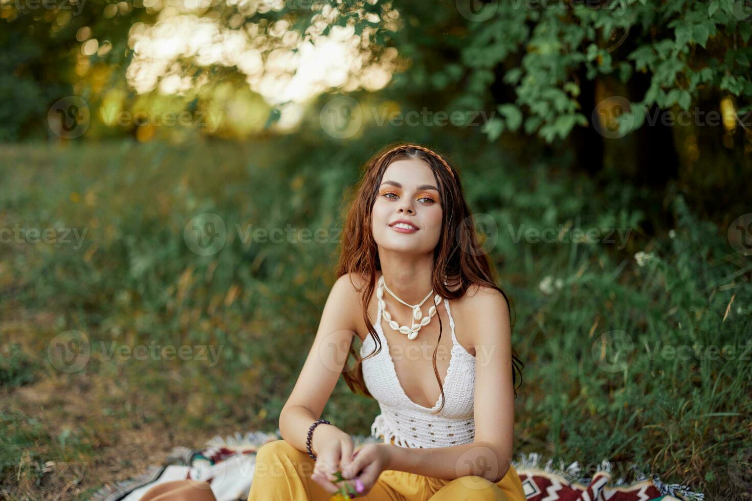 flicka klädd som en hippie eco avkopplande i de parkera, Sammanträde på en filt i de solnedgång, avslappnad livsstil foto