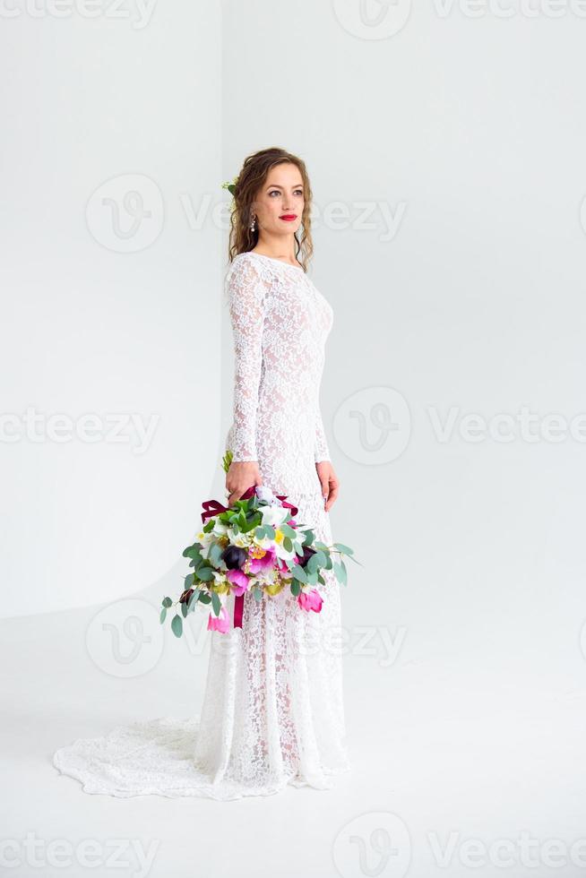 glad tjejbrud i en vit stickad klänning som poserar med en bukett blommor foto