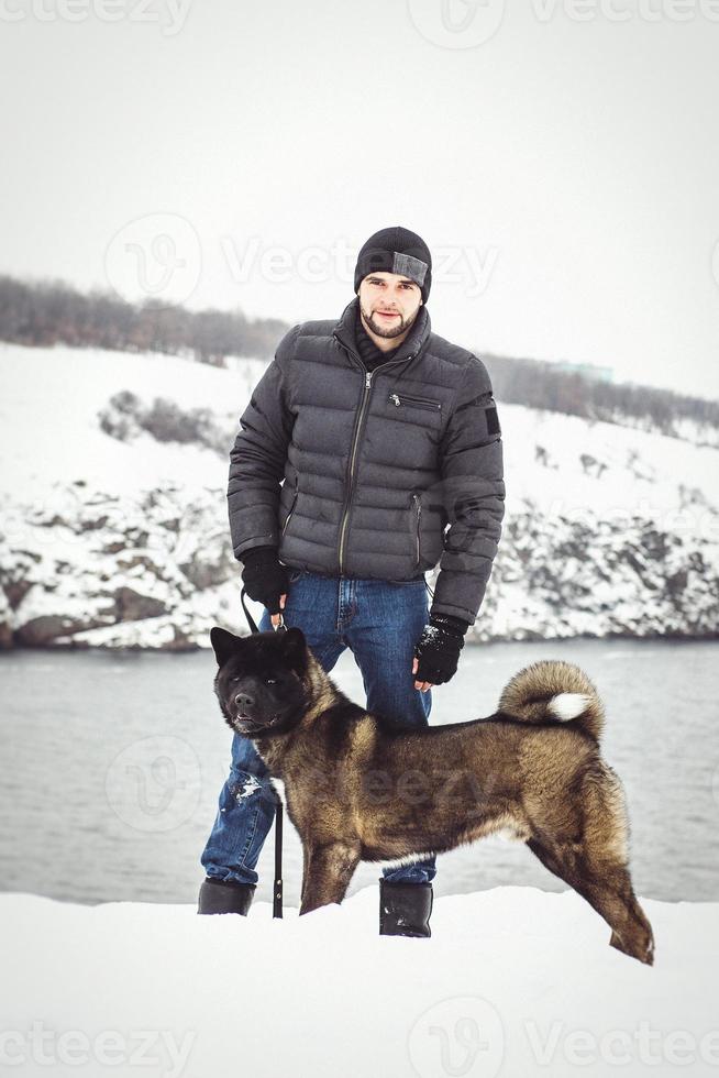 en man i en jacka och en stickad hatt går med en amerikansk akitahund foto